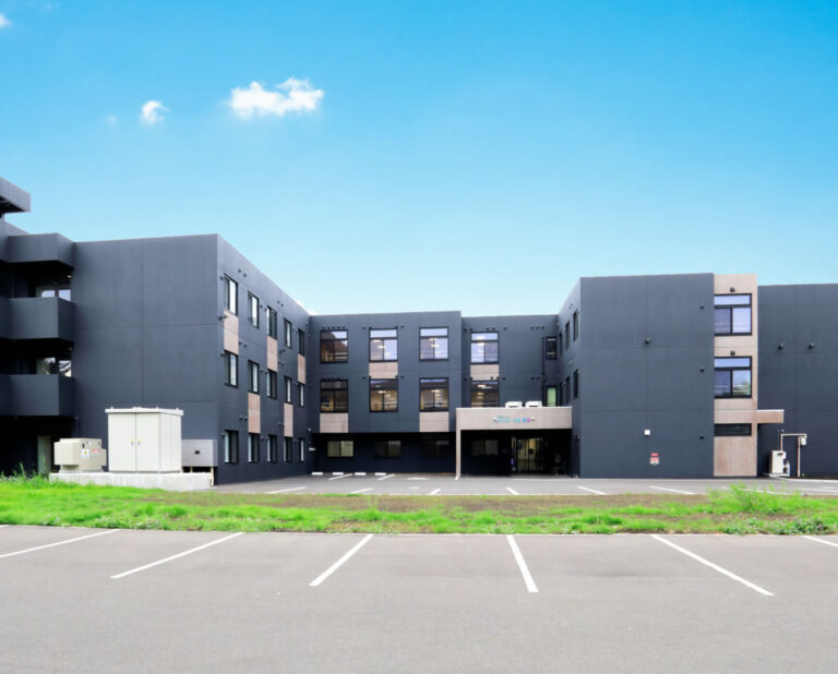 駐車場から見た介護施設の建物外観。モダンなグレー基調の多層構造。